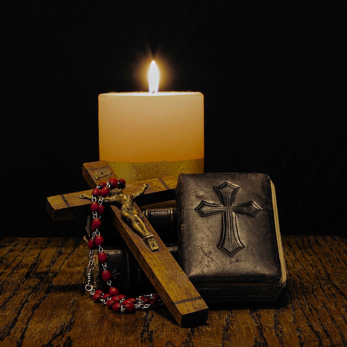 Lit candle beside a Crucifix, Rosary and prayer book