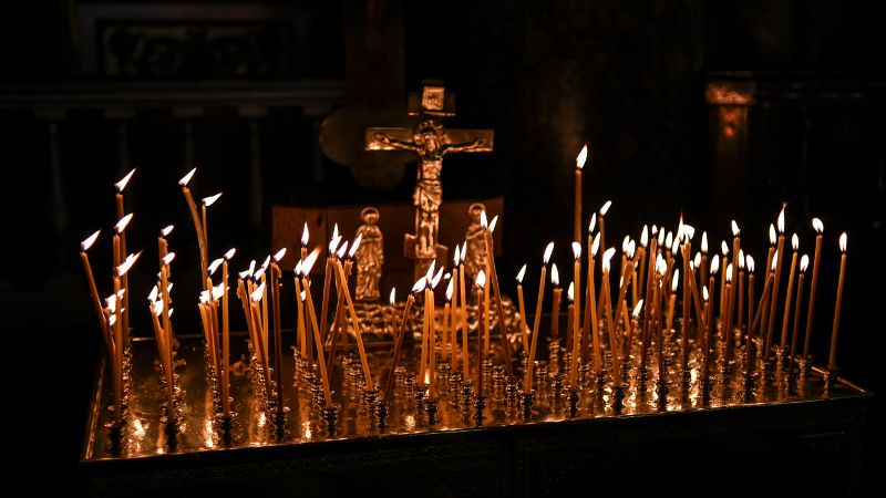 Many lit prayer candles before a Crucifix in a church